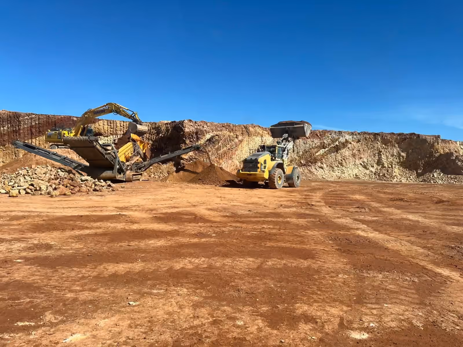 Excavator, mobile crusher and wheel loader working a red-earth open pit