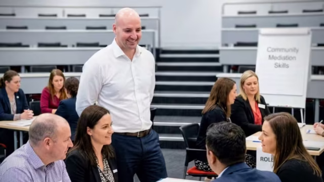 Thomas Gaultier leading a small-group exercise during a community mediation skills workshop, with participants working through a role-play scenario at round tables