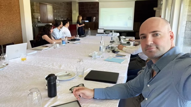 Thomas Gaultier participating in a stakeholder engagement workshop, seated at a conference table with a presenter and group of participants in the background